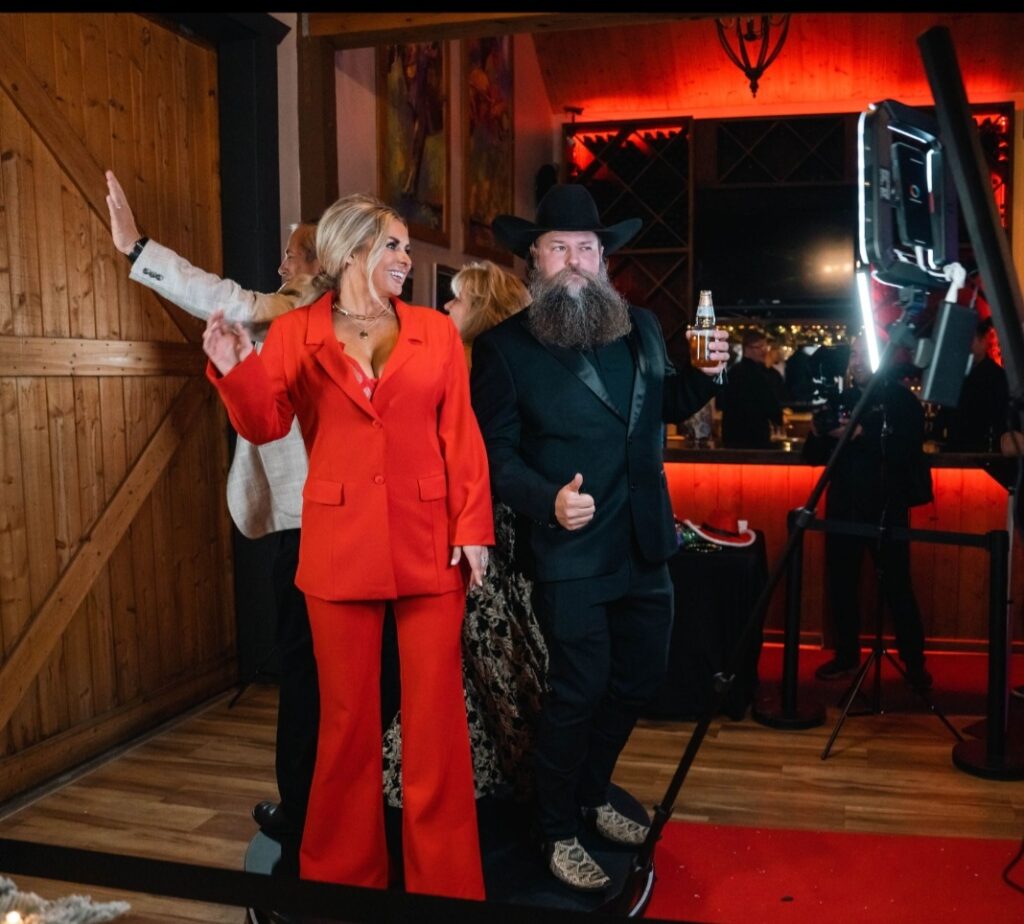 A group of people enjoying the immersive experience of a 360 video photo booth rental by Paloma Photo Booth near Temecula, CA. The booth features a circular design with multiple cameras capturing moments from every angle. Guests are seen striking poses, dancing, and expressing their excitement while being recorded in a 360-degree video format. Colorful LED lights illuminate the booth, adding a vibrant atmosphere to the scene. The Paloma Photo Booth logo is displayed prominently on the booth's exterior. The event venue is filled with captivating decorations, creating a visually stunning backdrop for the immersive photo booth experience.